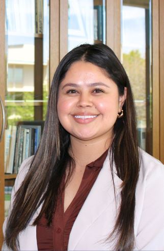 student smiling at the camera. There are bookcases in the background