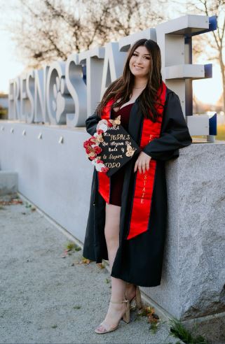 student in graduation attire. The Fresno State statue is in the background