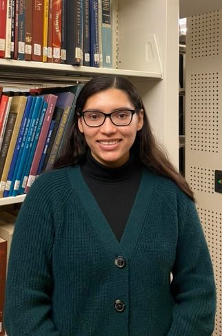 student smiling at the camera, bookstacks in the background