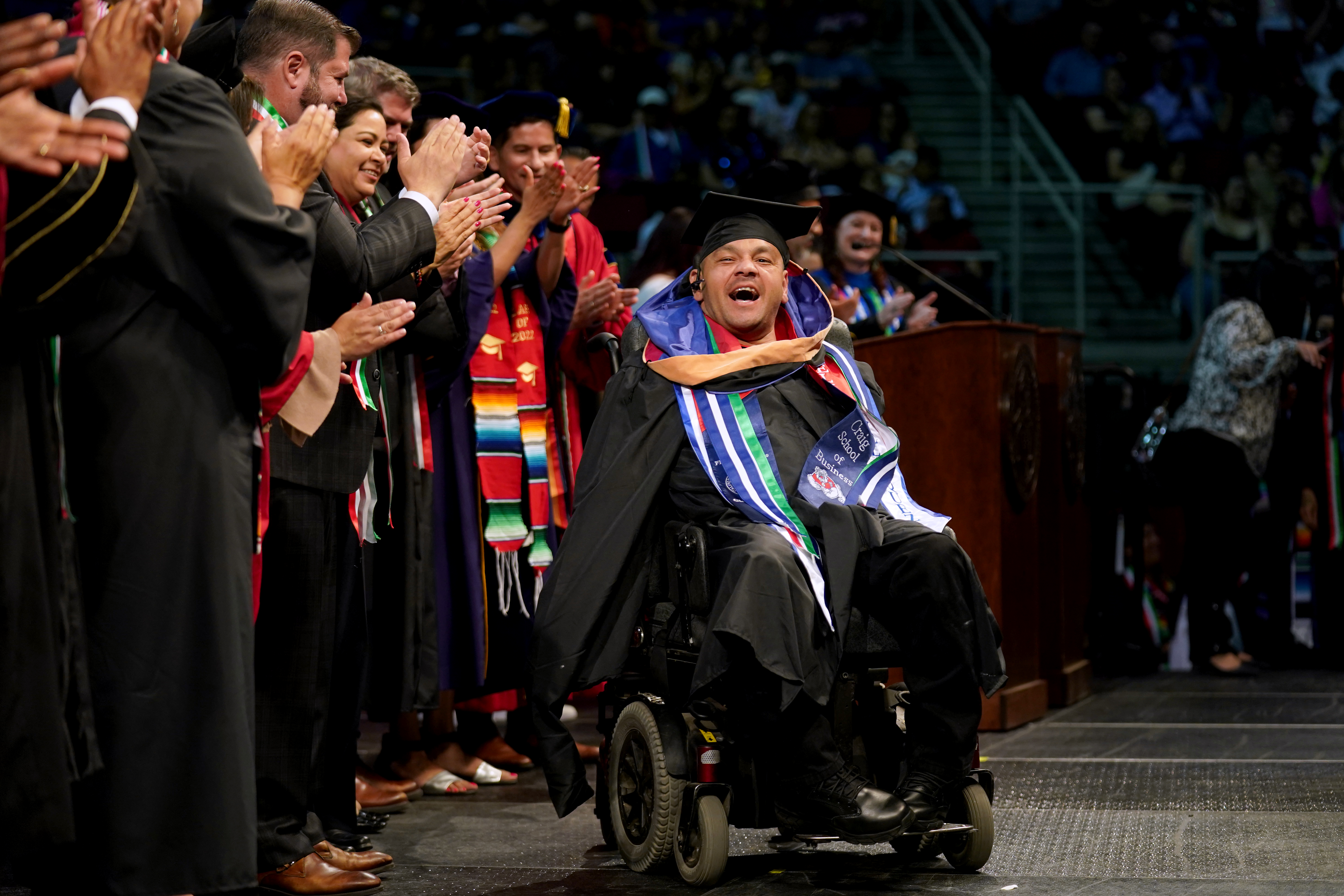 student in a wheelchair receives his masters hood at graduation ceremony